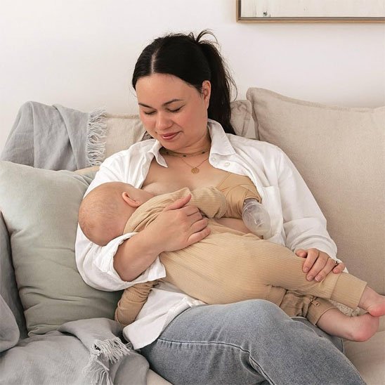 maman utilise tire-lait collecteur avec soutien-gorge pour tire-lait en allaitant bébé dans sofa